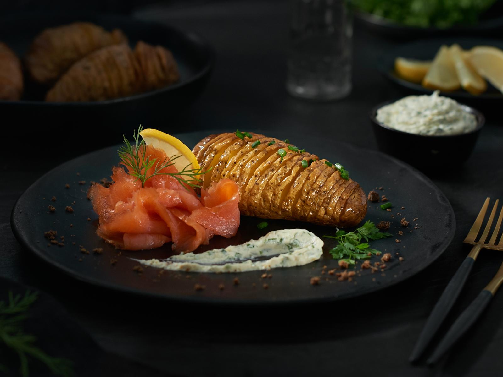 Hasselbackkartoffeln mit Räucherlachs Ein Teller mit einer gefächerten Backkartoffel und Räucherlachs mit Kräuterschmand
