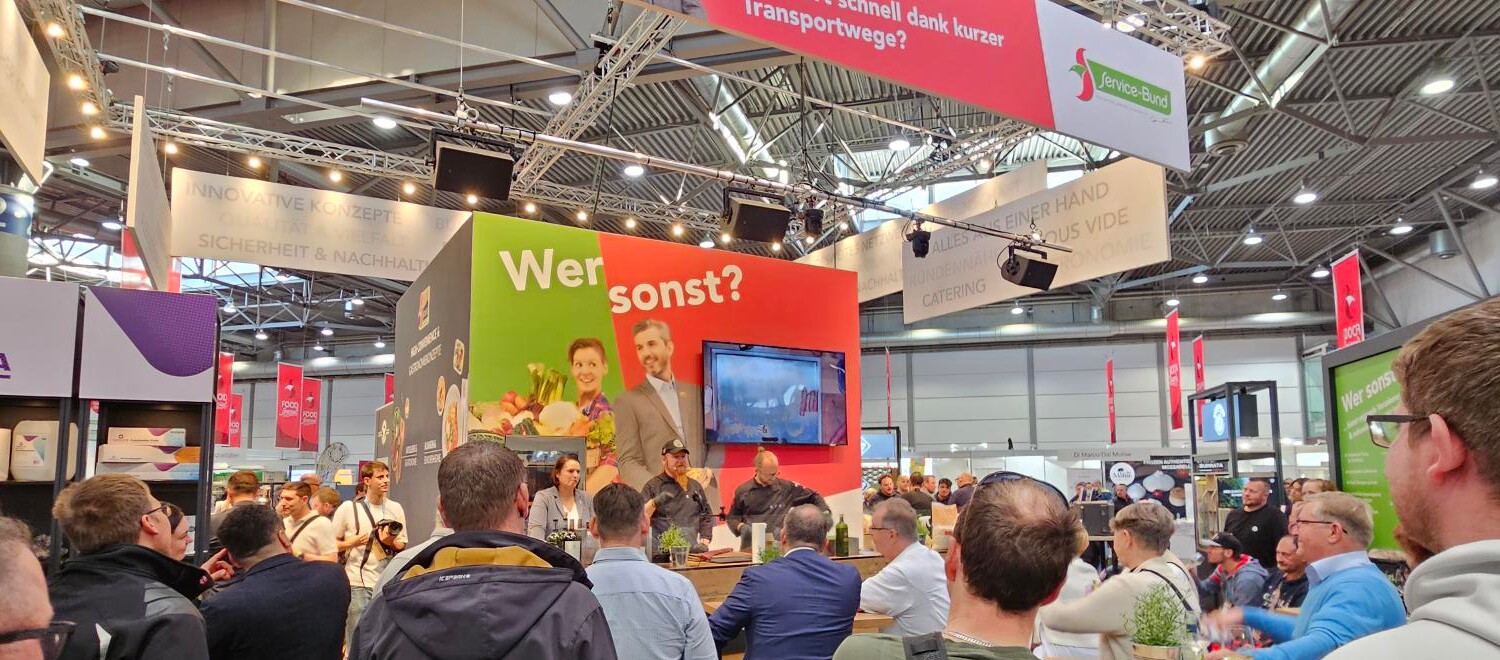 riationen Eine Gruppe von Menschen in einem Raum, darunter Männer und Frauen, die stehen und miteinander interagieren.