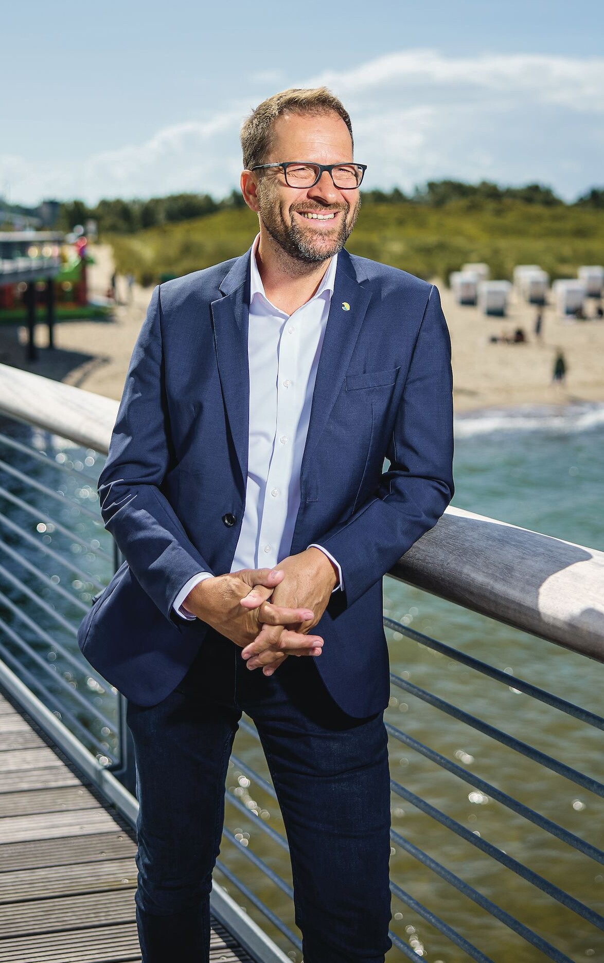 Ein Mann im Anzug lehnt an einem Geländer und lächelt.