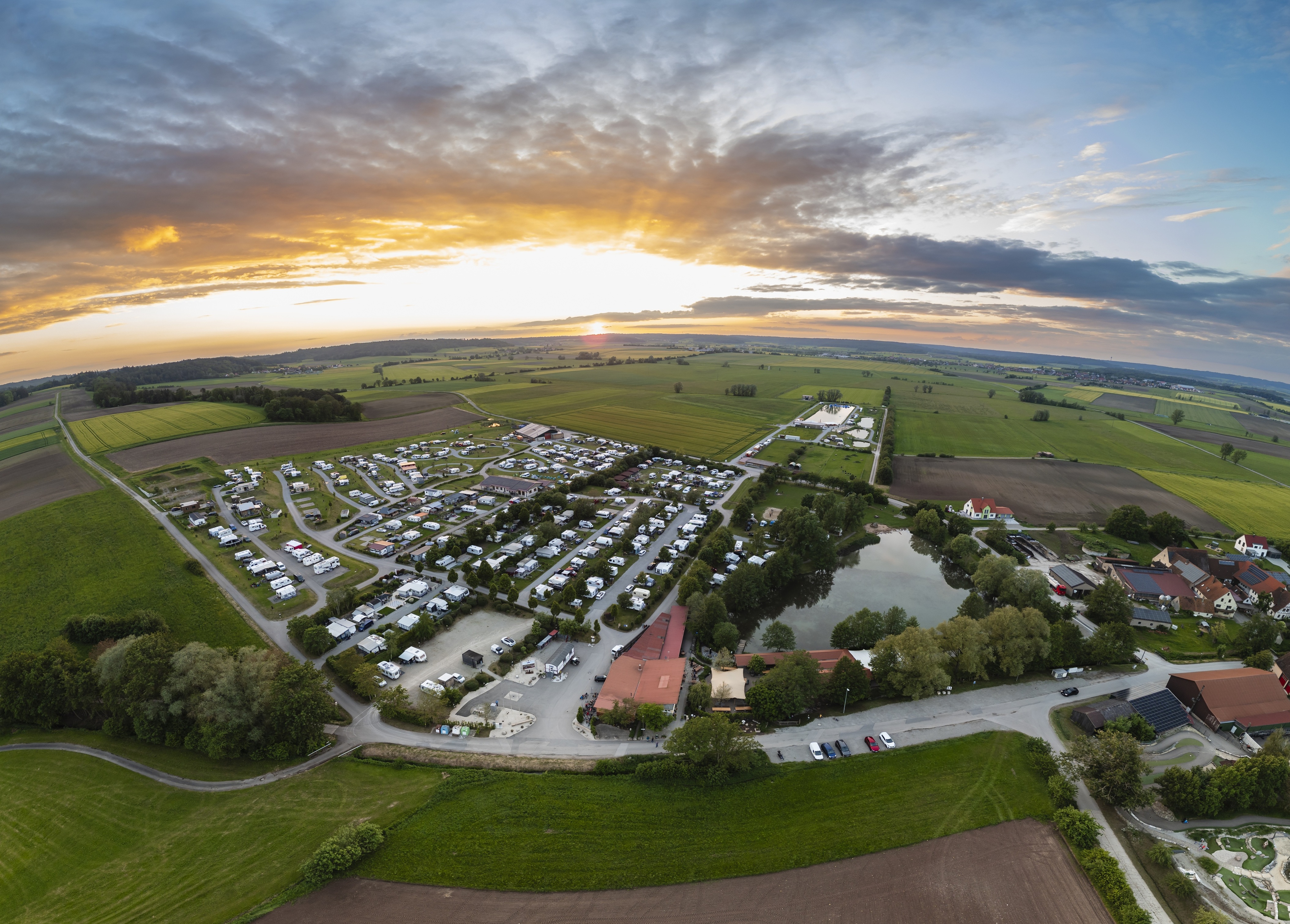 Das Freizeitparadies Mohrenhof aus der Vogelperspektive Luftaufnahme eines Campinsplatzes mit einem Teich und Sonnenuntergang