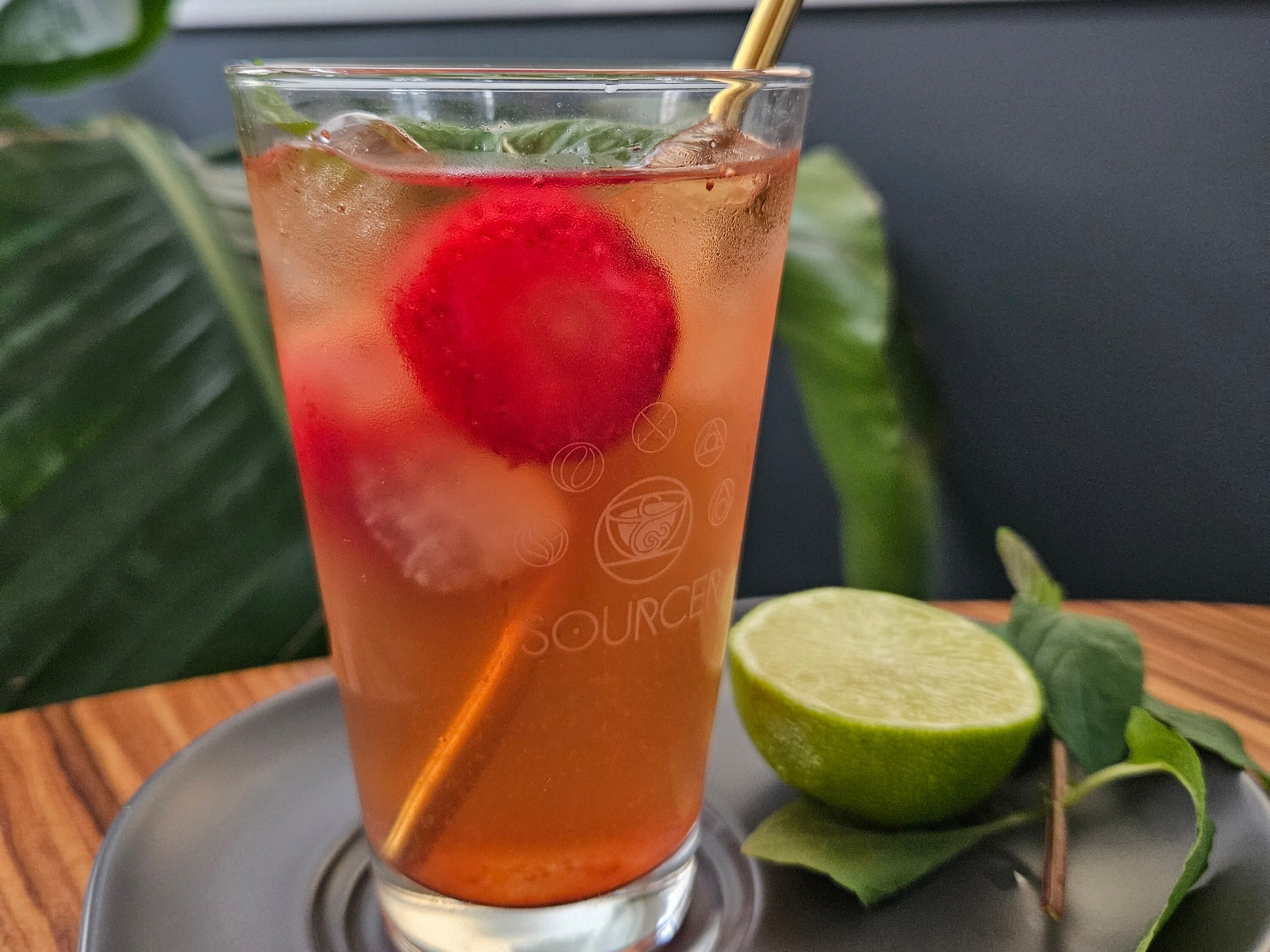 Ein Glas Eistee mit Strohhalm und einer Limette auf einem Teller.