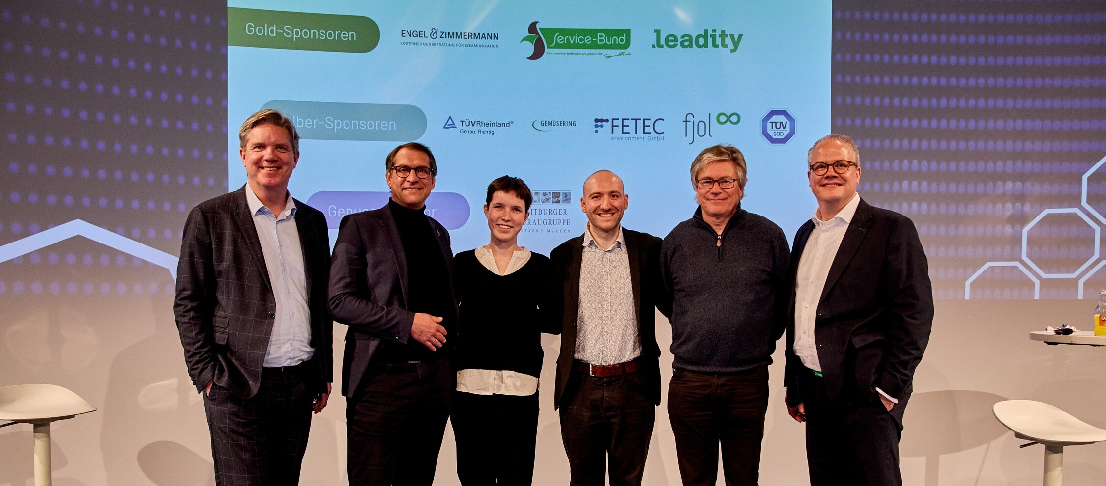 Eine Gruppe von Menschen steht vor einem großen Bildschirm.