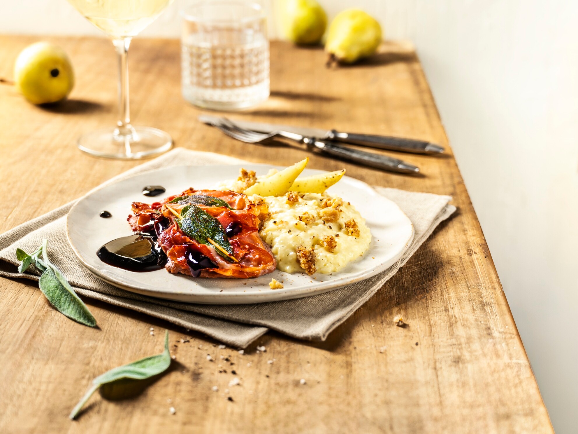 Ein Teller mit Risotto, Saltimbocca und Birnenspalten auf einem Tisch.