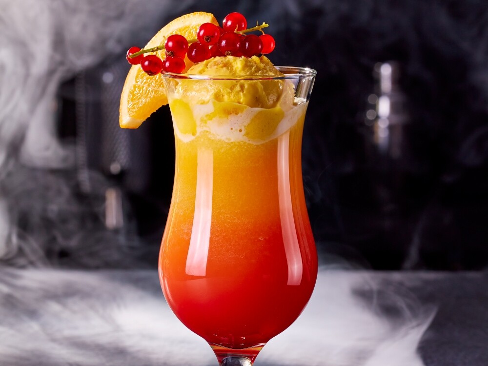 Better Desserts Tequlia Sunrise Ein Glas mit einem Cocktail und einer Fruchtgarnitur.
