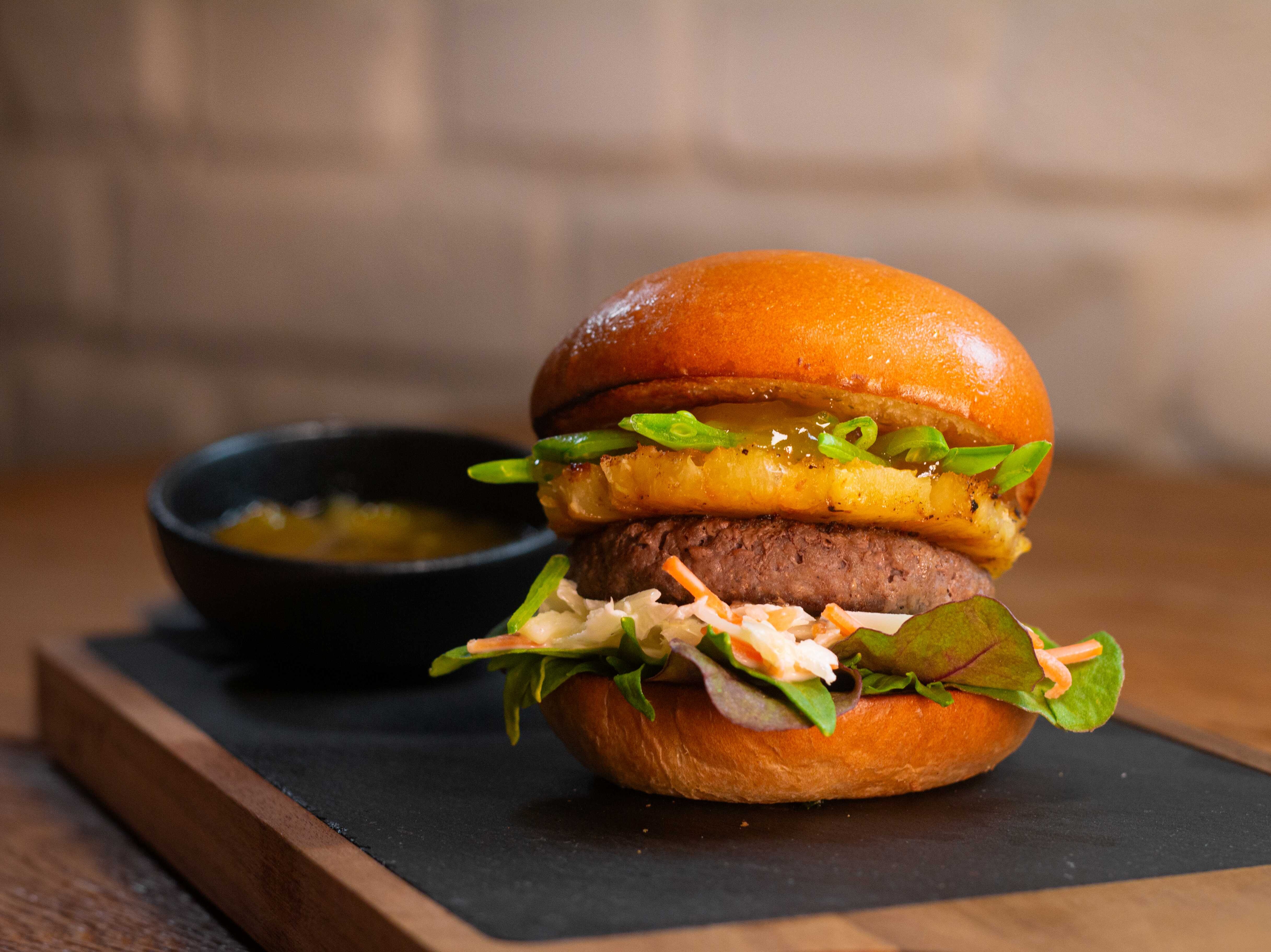 Burger mit Ananas und Salat auf schwarzer Oberfläche Burger mit Ananas und Salat