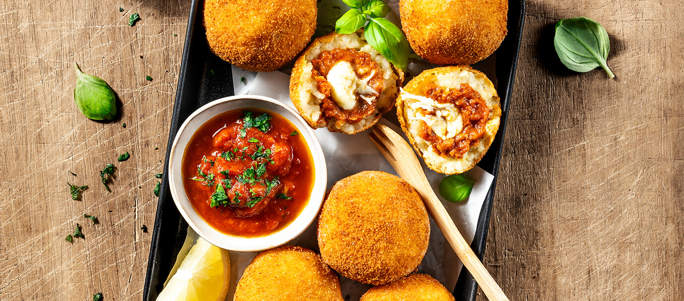 Arancini: Frittierte Reisbällchen aus Sizilien Ein Teller mit frittierten Reisbällchen, Saucen und Zitronen.