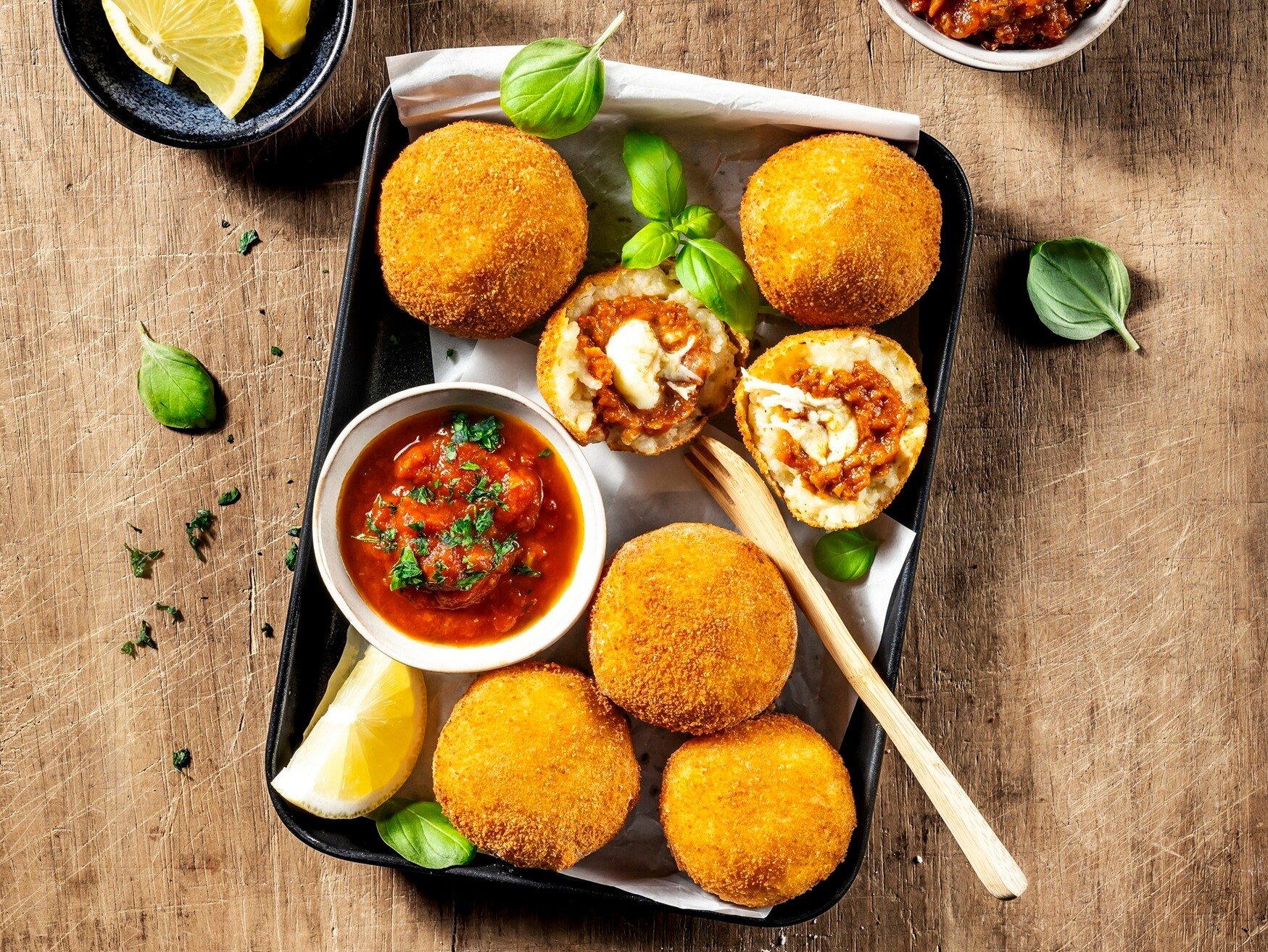 Ein Tablett mit frittierten Risotto-Bällchen, Saucen und Zitronen.