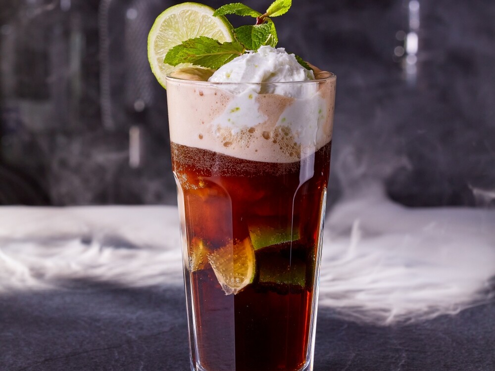 Ein Glas mit einem Cocktail und einer Fruchtgarnitur.
