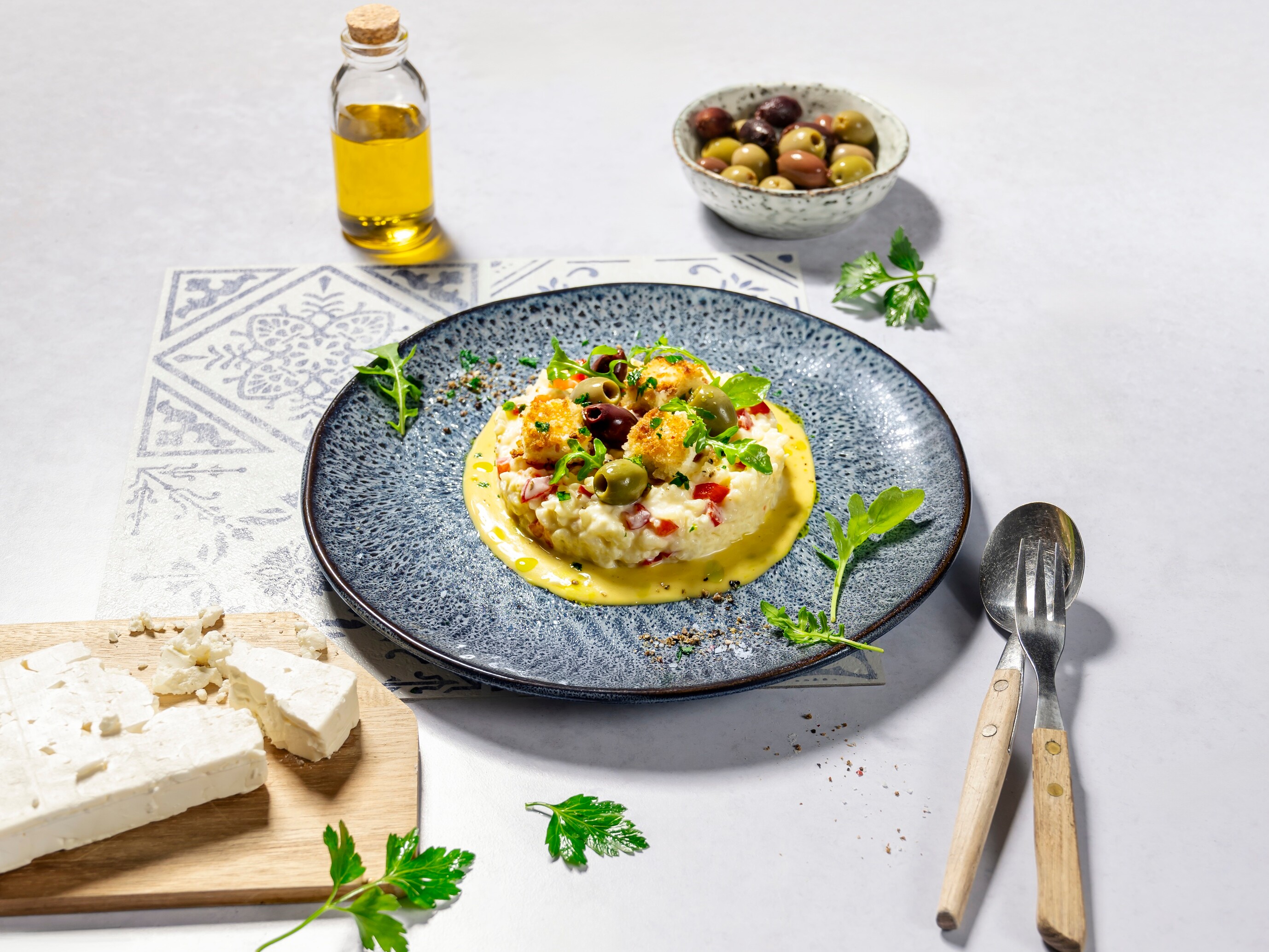 Ein Teller mit Risotto und Oliven, Schafskäse, Olivenöl auf einem Tisch.