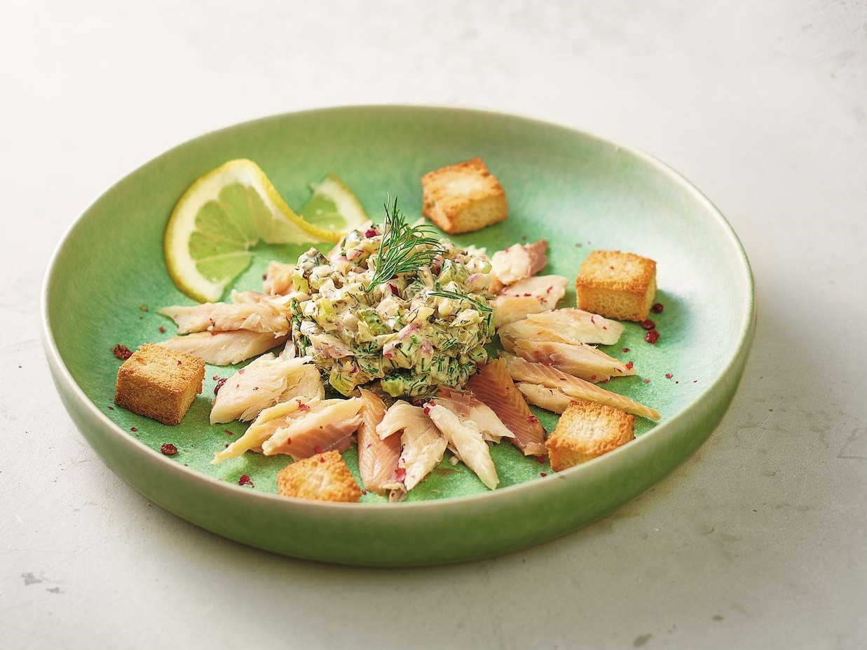 Pulled Räucherfisch mit Pickle-Tatar Ein Teller mit Räucherfisch und Gewürzgurkentatar, garniert mit Zitrone.