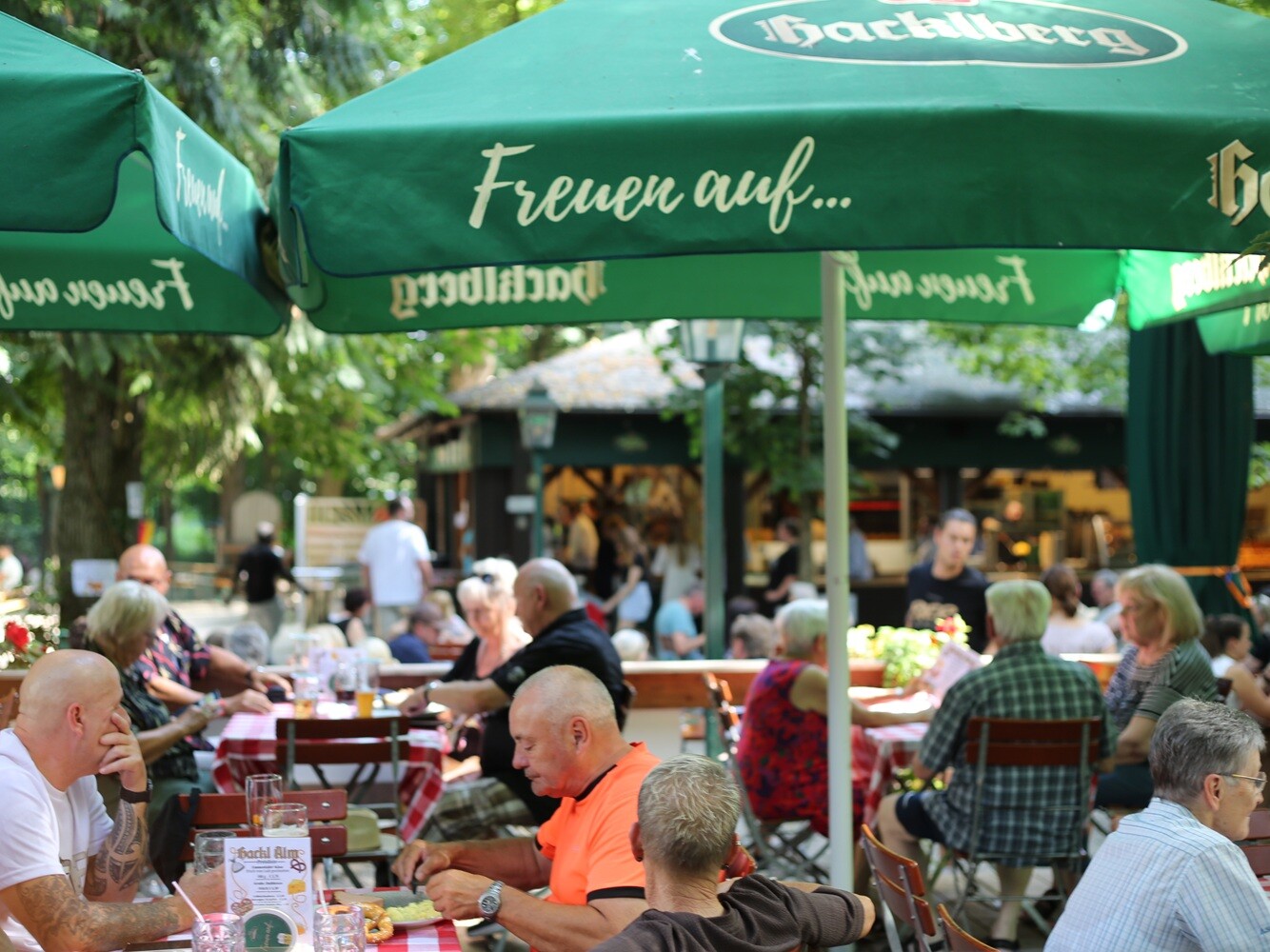 Eine Gruppe von Menschen sitzt an Tischen unter Sonnenschirmen im Freien.
