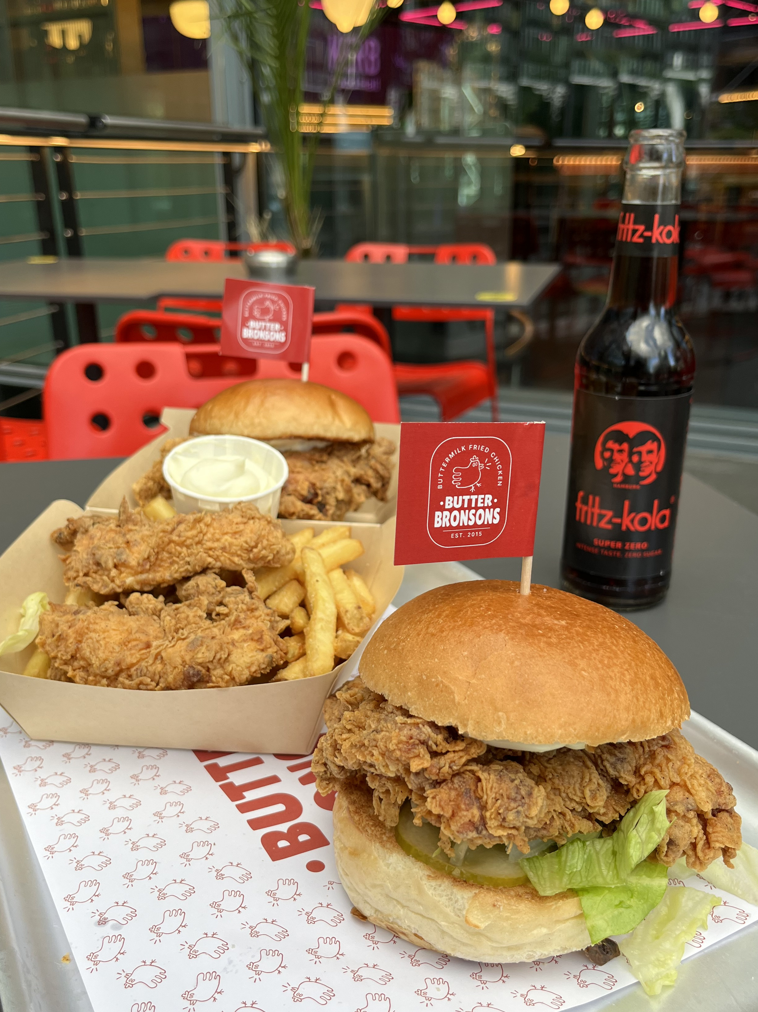 Ein Tablett mit Fast Food, darunter ein Cheeseburger und ein Getränk, auf einem Tisch.