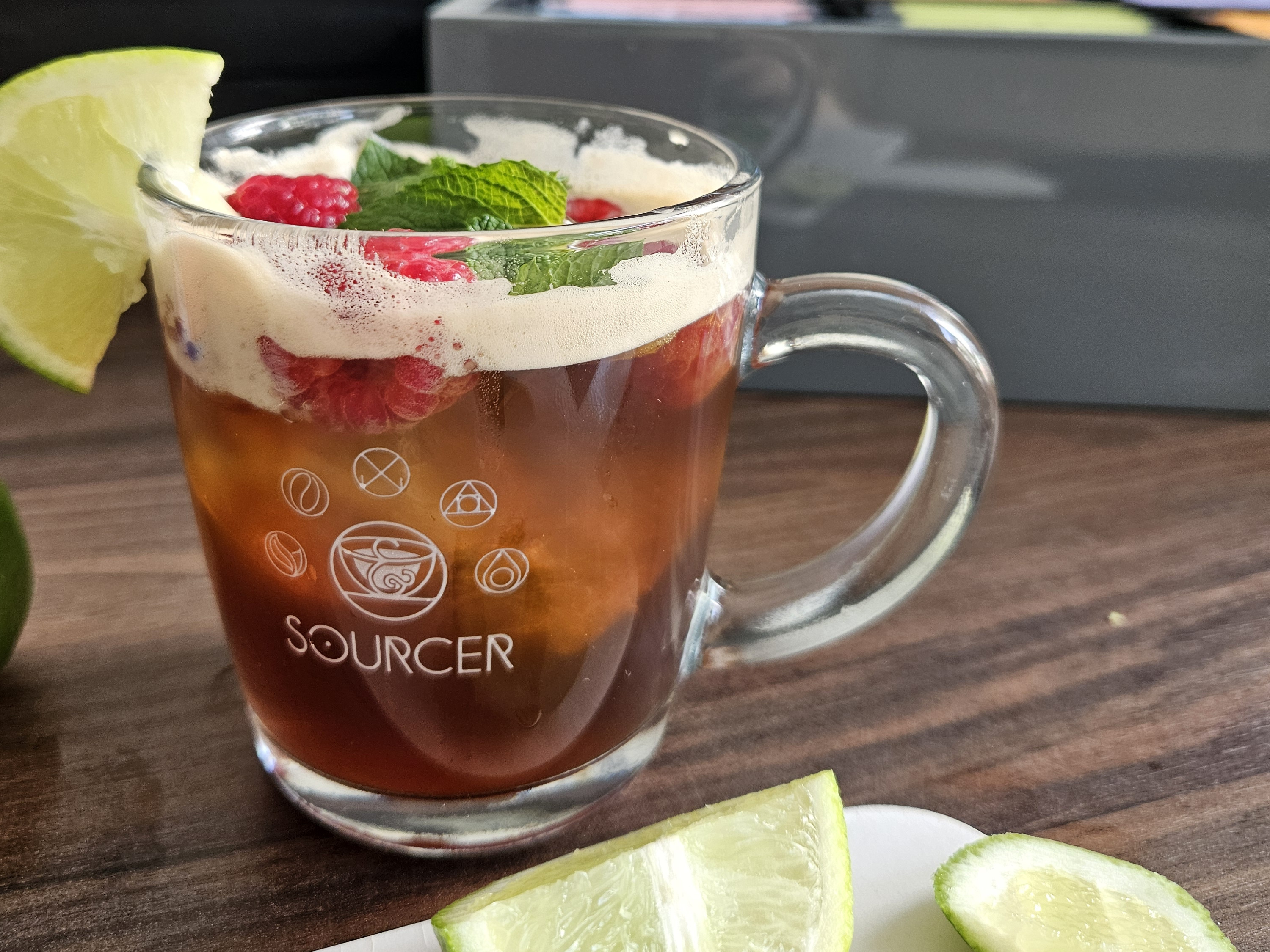 Ein Glas Tee mit Limette und Himbeeren auf einem Tisch.